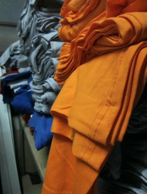 Stacks of orange, gray, and blue T-shirts manufactured in batches